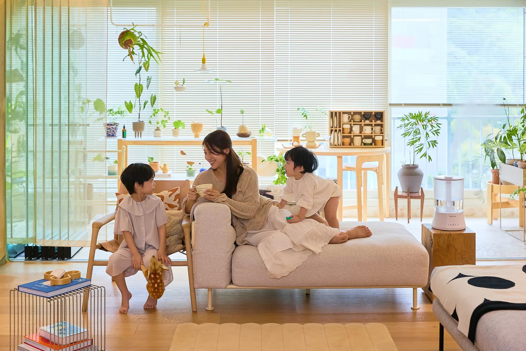 햇살이 드는 거실 소파에서 엄마와 두 아이가 웃으며 이야기하고, 옆 나무 탁자 위에 브링더홈 가습기가 놓인 모습